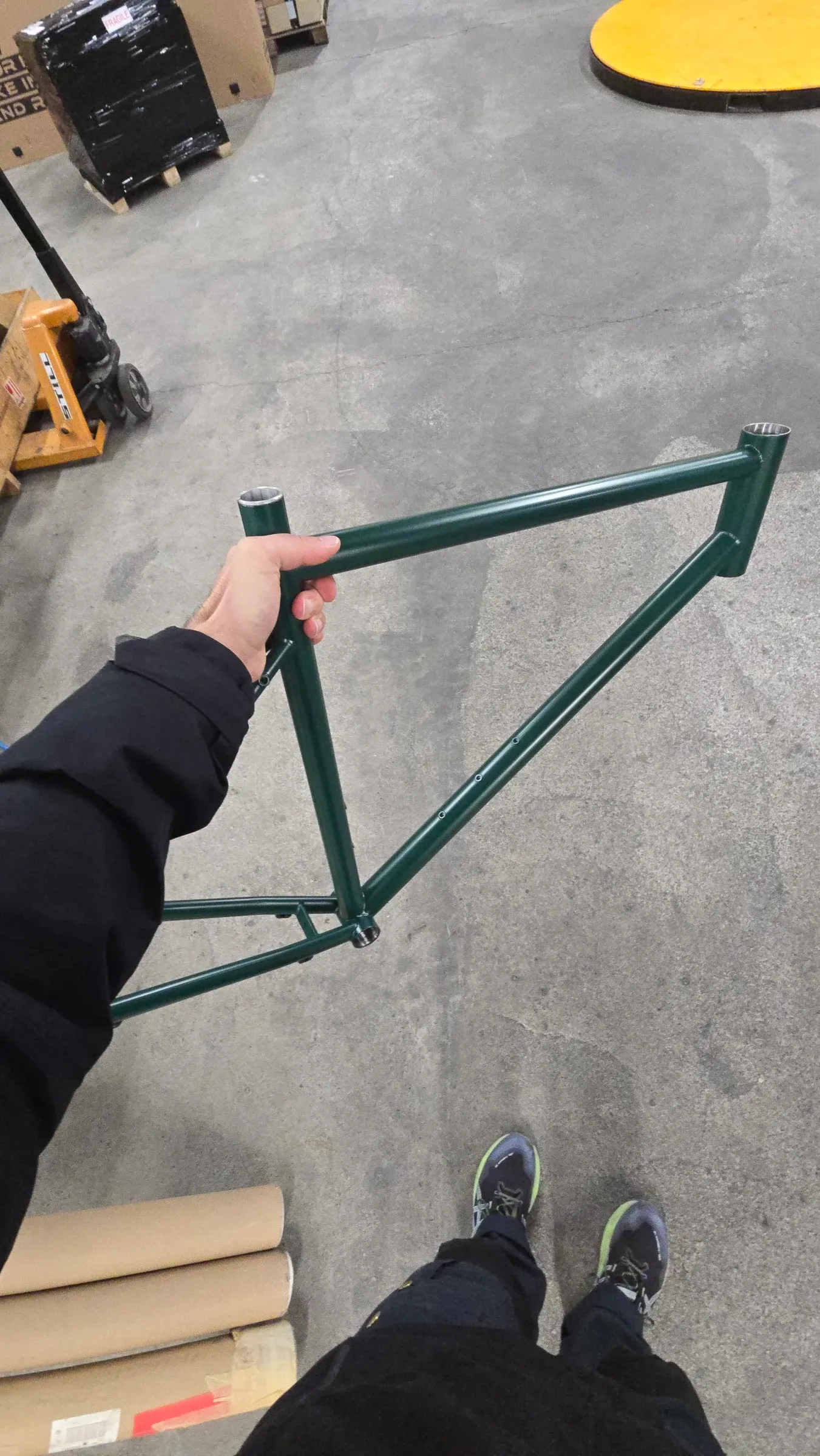 Cadre Racine vert mousse tenu à bout de bras dans un atelier, vue plongeante