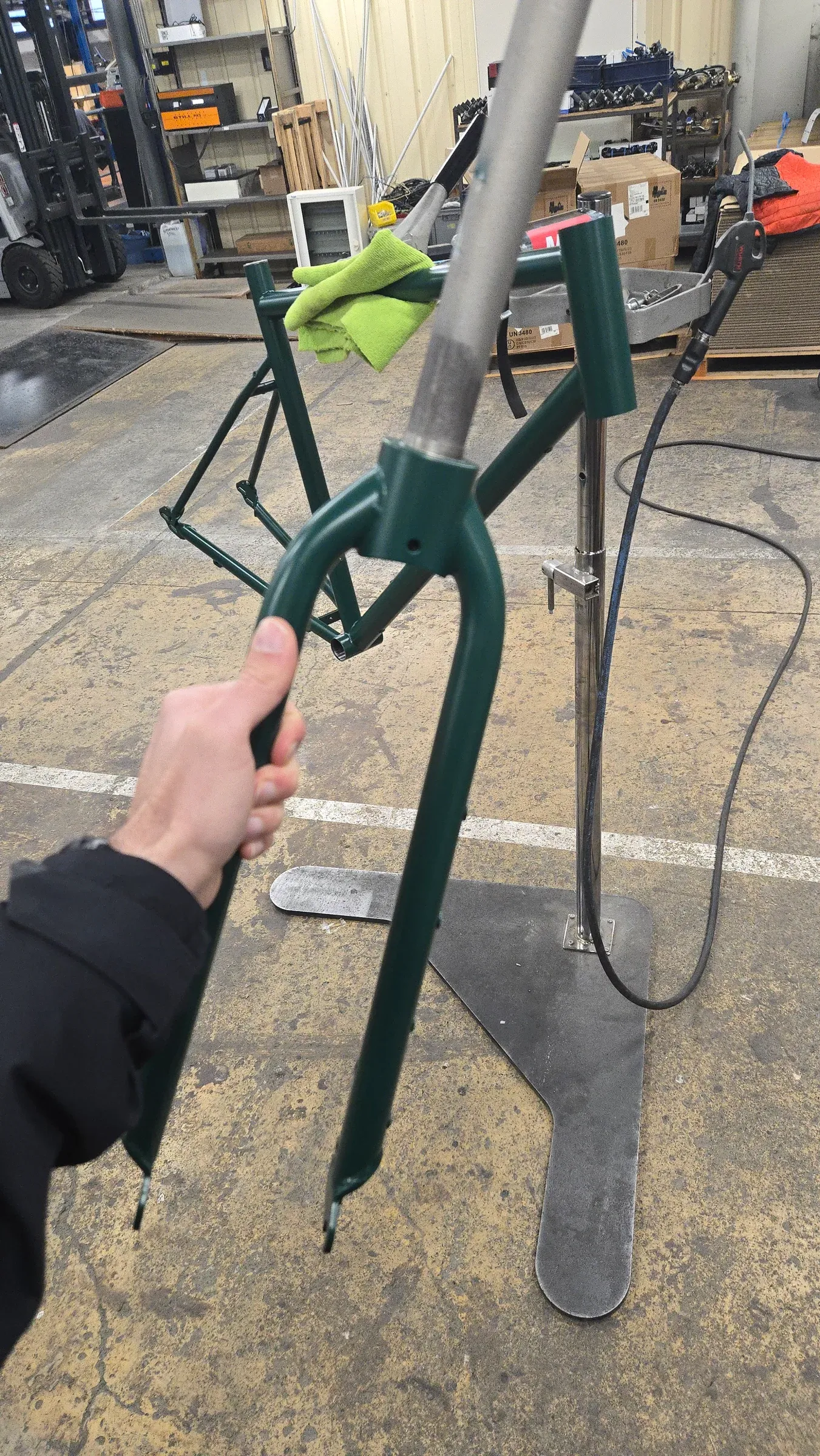 Fourche Racine vert mousse tenue à la main devant un cadre thermolaqué de la même teinte