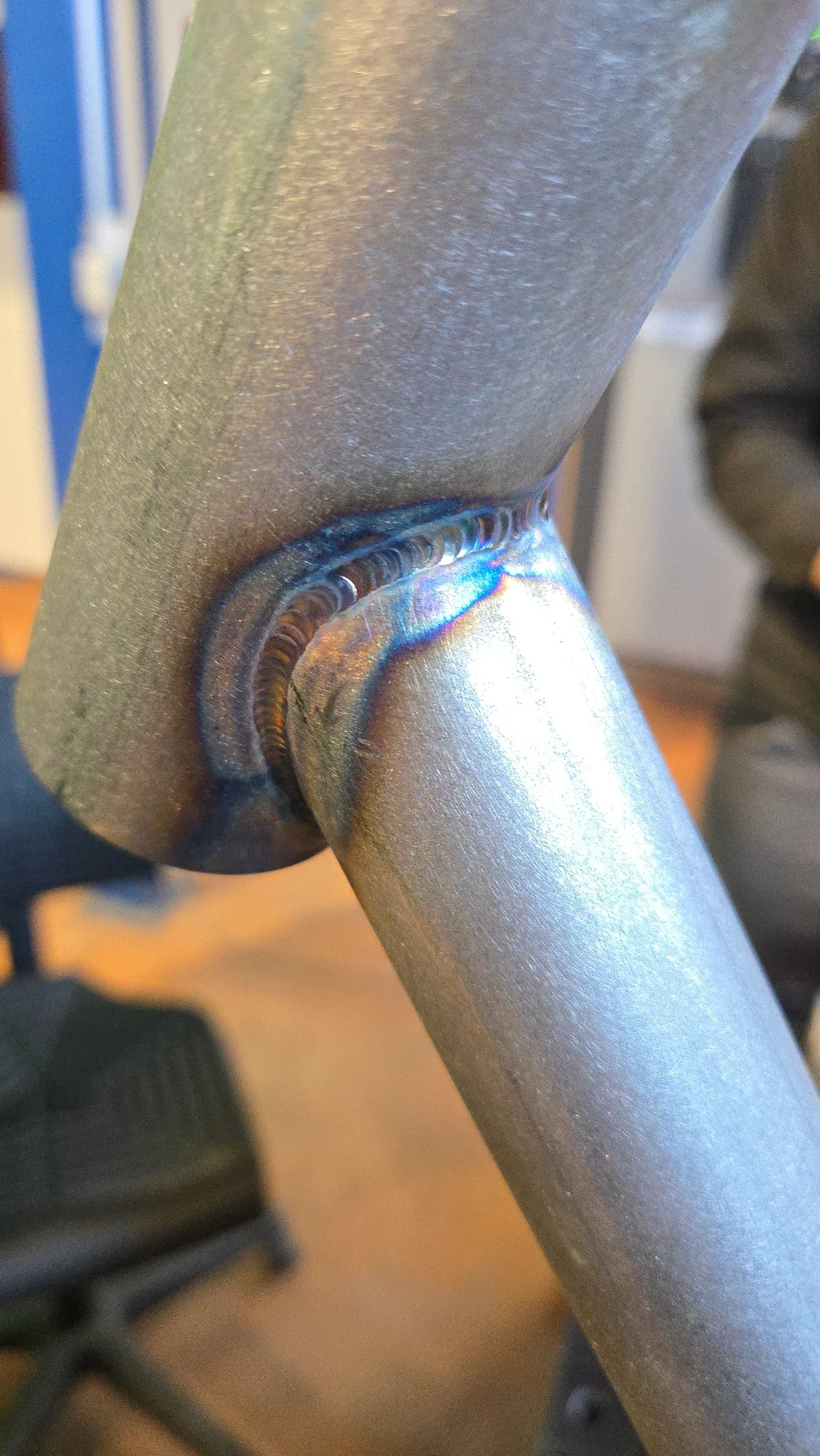 Gros plan sur un cordon de soudure TIG entre deux tubes d'acier, teintes de revenu bleutées et cuivrées