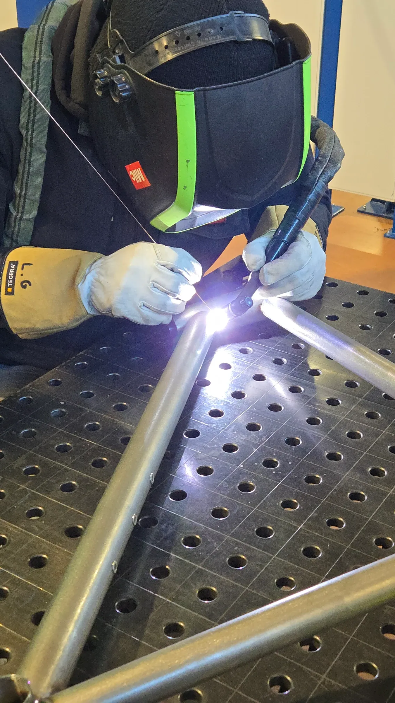 Soudeur en gants de cuir soudant à l'arc TIG deux tubes d'acier bridés sur une table de soudure perforée