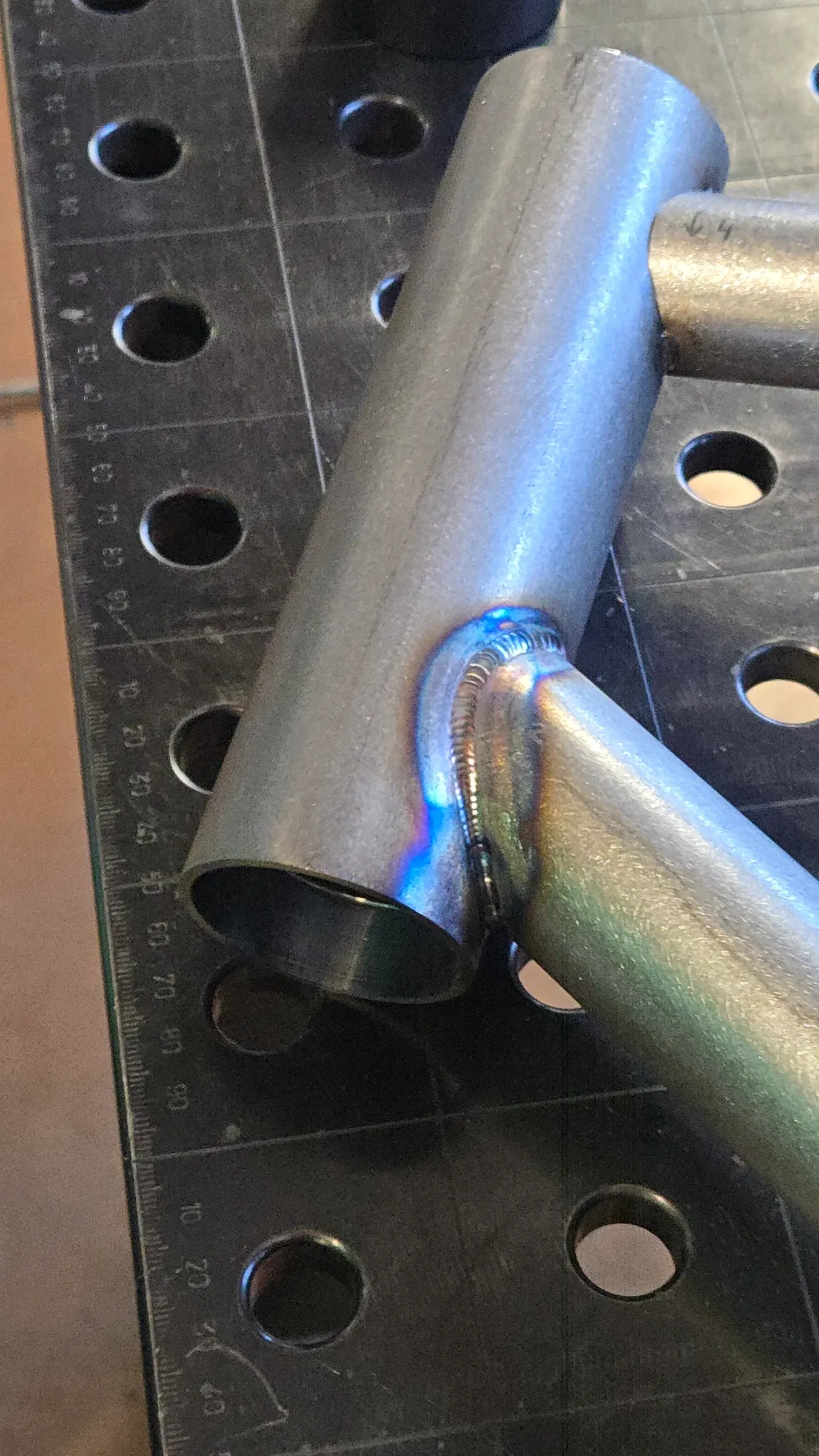 Cordon de soudure TIG entre deux tubes d'acier, teintes de revenu bleutées, sur table de soudure
